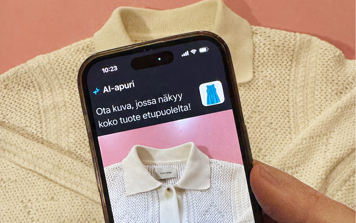 Kermanvärinen neulottu poolopusero ja sen edessä käsi, joka pitelee älypuhelinta, jonka näytöllä näkyy kuva samasta puserosta vaaleanpunaisella taustalla.